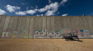a concrete wall with graffiti stands on desert sand against blue sky