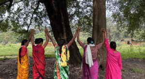 Five women holding hands standing in front of a tree