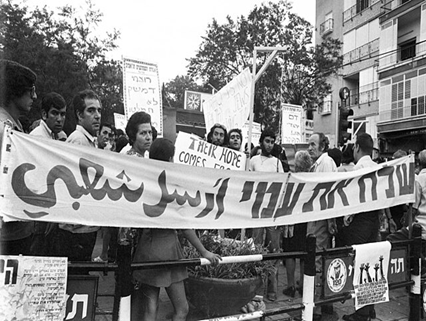 Black-and-White picture with Israelis demonstrating against the persecution of Jews in Syria and Iraq in 1973. Protestors in the first row hold a huge banner with a slogan in Hebrew and Arabic. It reads “Let my people go.”