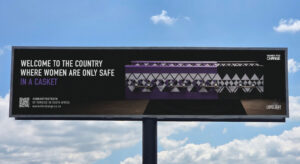 Bilboard on the highway from the women's rights organization ‘Women For Change’. It shows a purple and white patterned coffin with the inscription: ‘Welcome to the country where women are only safe in a casket’.