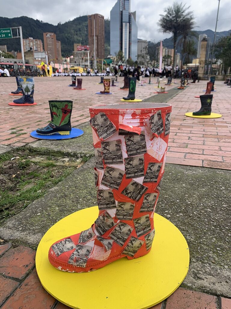 Public square in which boots that are decorated with various items like photos or images are exhibited. The background shows a skyline of highrise buildings and mountains