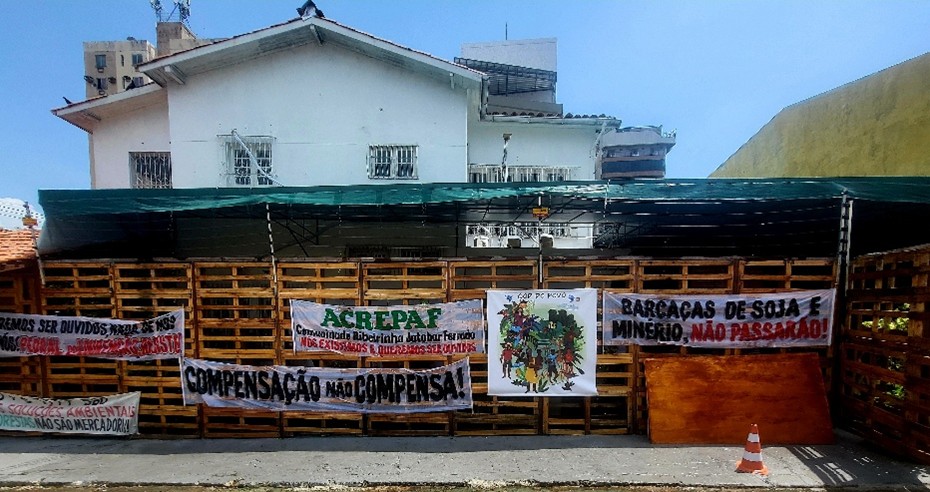 Bild des Hauses 'COP DO POVO' ("COP des Volkes"): Zu erkennen ist das Obergeschoss eines weißen Gebäudes, das sich hinter einem überdachten Holzzaun befindet. Am Zaun hängen Protestbanner zivilgesellschaftlicher Gruppen mit portugiesischer Aufschrift.