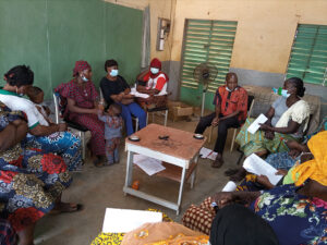Group of people sitting in a circle on chairs in a room, some of them are wearing medical masks.