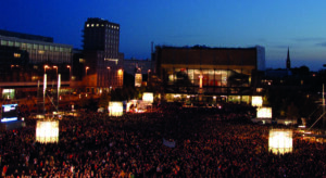 Menschenmassen auf dem Augustplatz in Leipzig am Abend: Gedenkfeier am 9. Oktober 2009 anlässlich des 20. Jahrestags der Friedlichen Revolution; im Hintergrund hohe Gebäude und der dunkle Abendhimmel zu sehen; auf dem Hochhaus rechts steht eine 89