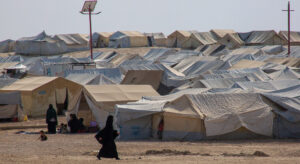 Camp made up of tents, a veiled person walks past in the foreground.