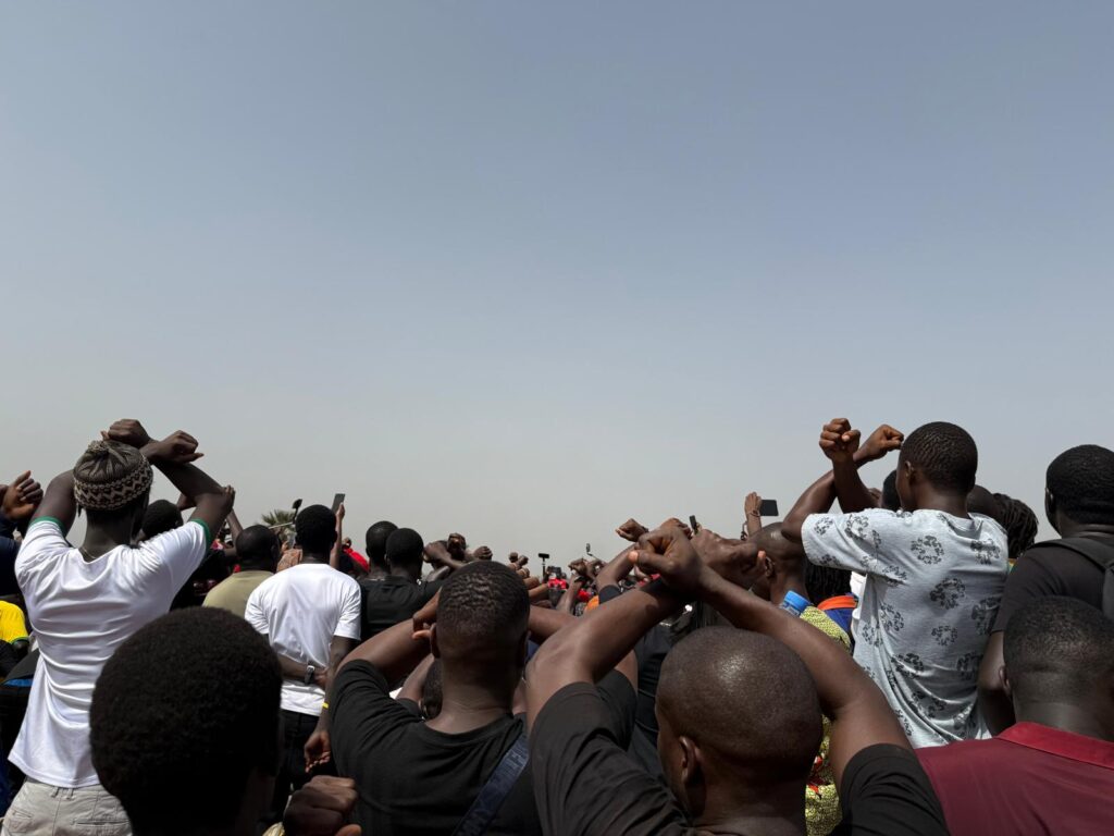 Back view of a crowd of people. They make a gesture in which their forearms are crossed and their hands are clenched into fists.
