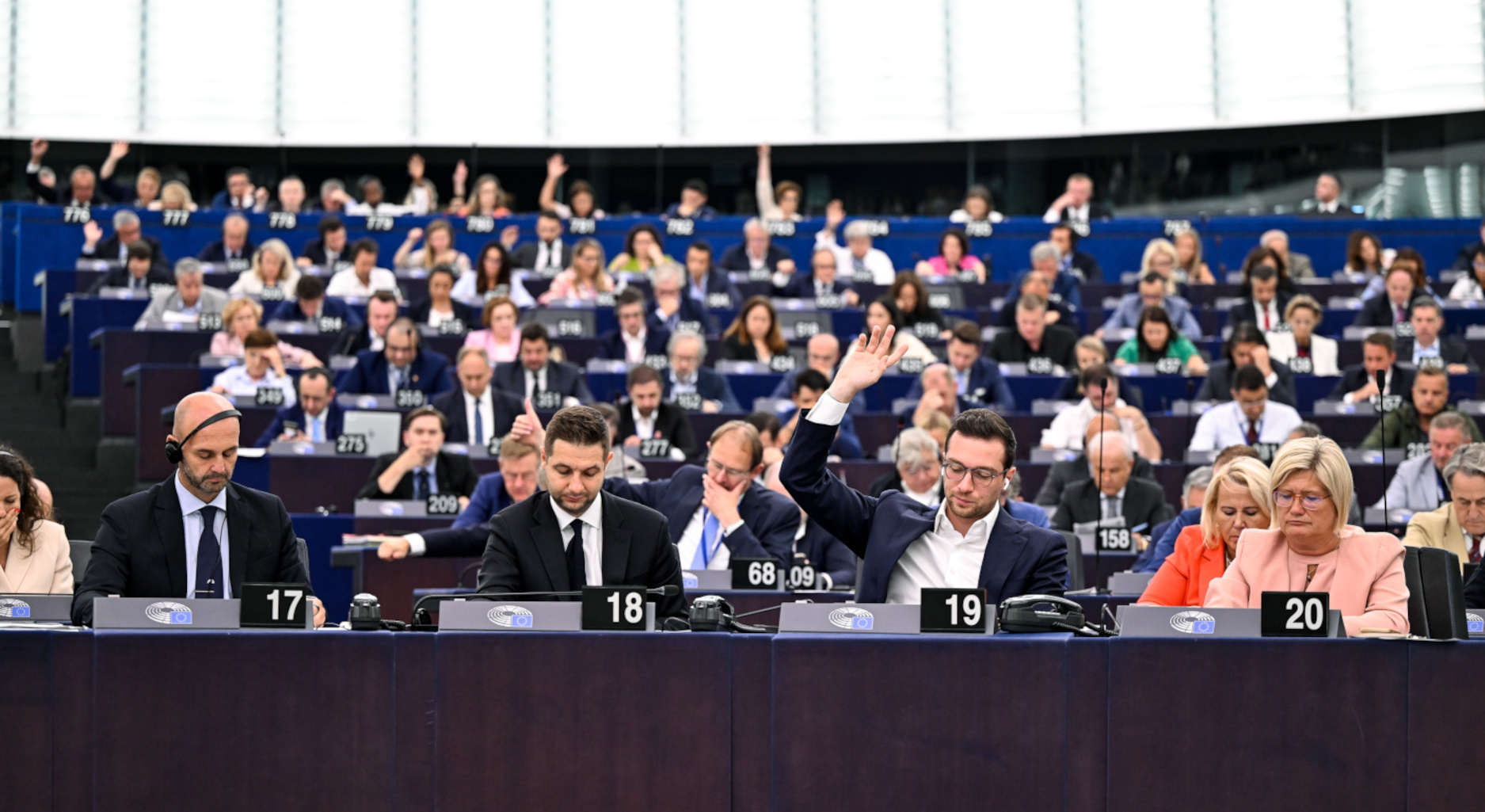Mehrere Personen sitzen in einer Plenarsitzung des Europäischen Parlaments, eine Person hebt die Hand zum Abstimmen