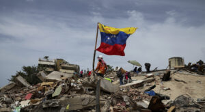 People on rubble with a waving Venezuelan flag under a cloudy sky